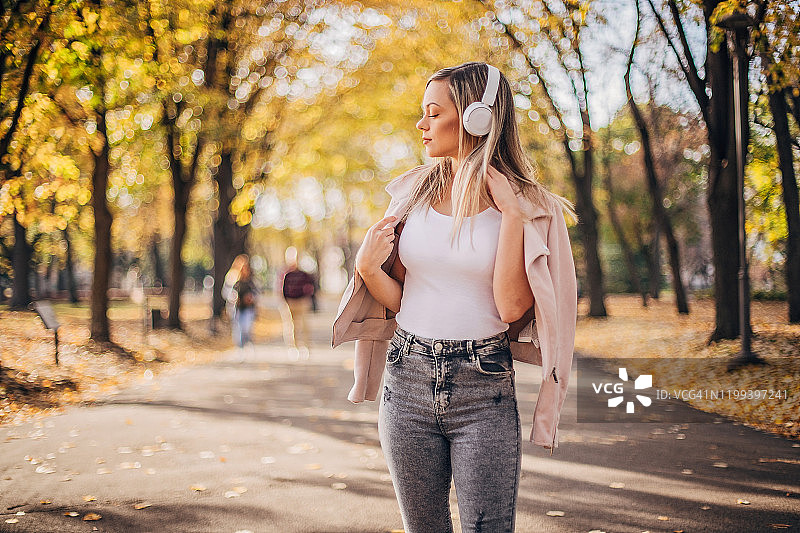 一个女人在公园里散步，戴着耳机听音乐图片素材