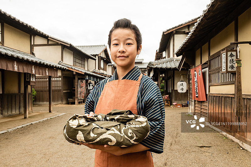 一个穿着老式衣服的日本男孩在乡村街道上拿着一个包装好的包裹图片素材