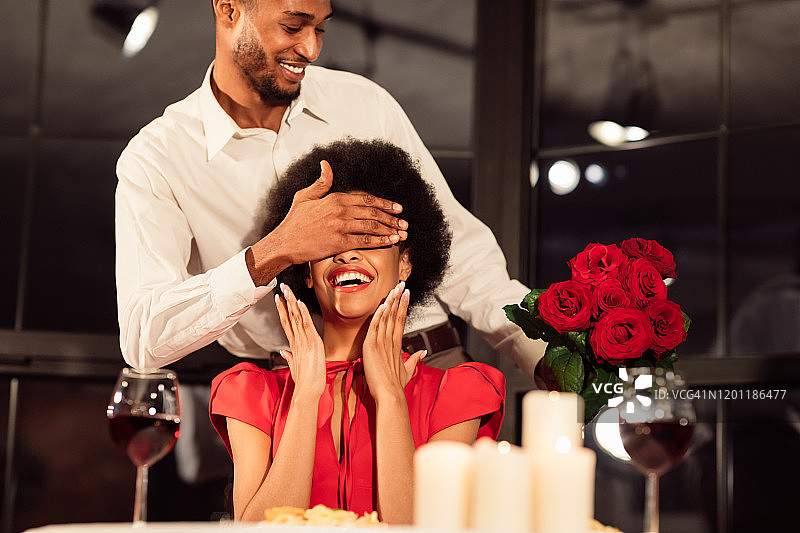 在饭店里，男人捧着花束遮住女人的眼睛庆祝情人节图片素材