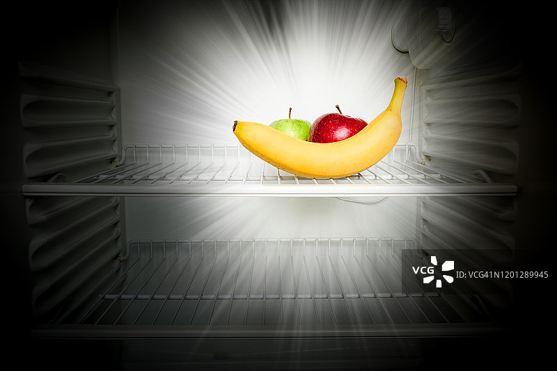 新鲜的红绿苹果和香蕉在黑暗中发光的概念创意照片在一个开放的空冰箱。减肥饮食概念。图片素材