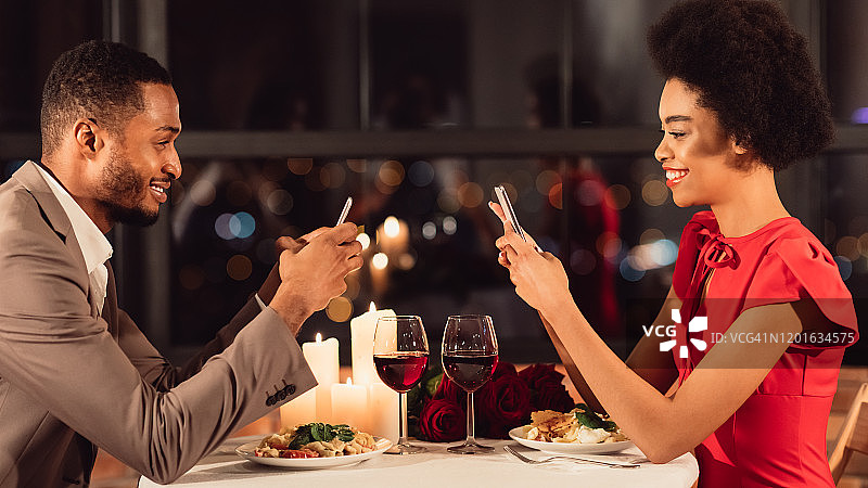 非洲裔情侣在餐厅浪漫约会时使用智能手机图片素材