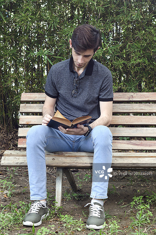 一个年轻人坐在花园里的长凳上看书图片素材