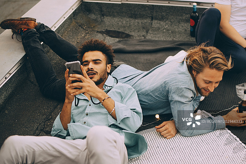 高角度的人使用手机，而躺在露台上的朋友在屋顶派对图片素材