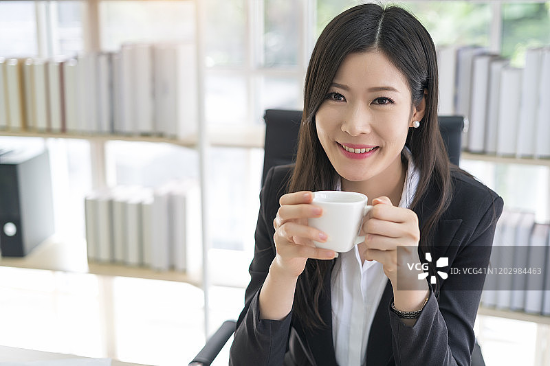 微笑的商务女性在现代的办公室里喝咖啡休息图片素材