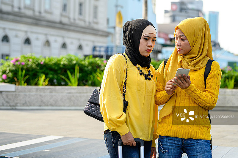 两名年轻的穆斯林妇女戴着头巾自拍与她的智能手机在城市街道上图片素材