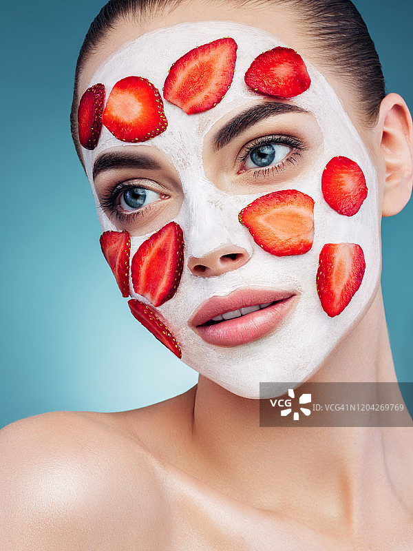快乐的年轻女孩面膜和草莓片在她的脸上图片素材