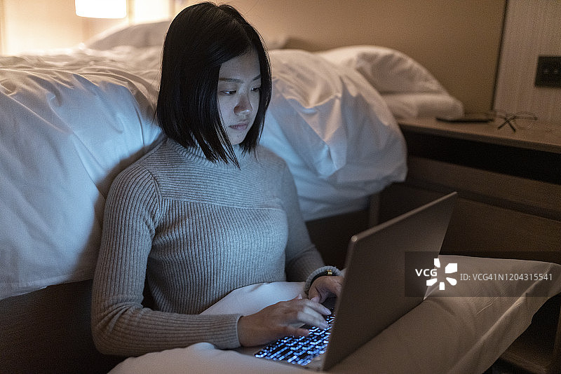 亚洲女性晚上在卧室用笔记本电脑工作图片素材