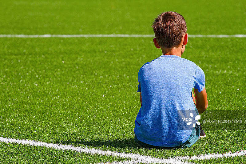 悲伤孤独的男孩坐在足球场外的露天体育场图片素材
