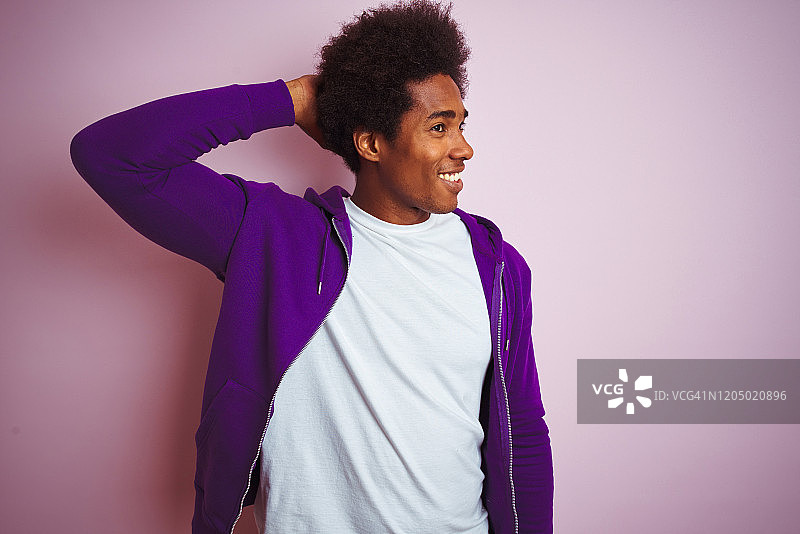 年轻的非洲裔美国人穿着紫色运动衫站在孤立的粉红色背景微笑自信触摸头发与手向上的手势，摆出有吸引力和时尚的姿势图片素材