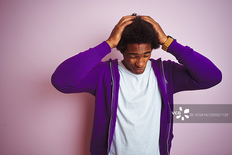 年轻的非洲裔美国人穿着紫色的运动衫站在孤立的粉红色背景下忍受着头痛绝望和压力因为疼痛和偏头痛。手放在头上。图片素材