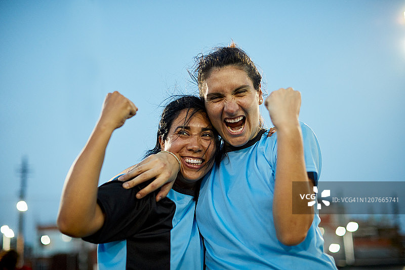 两名女子足球运动员举起拳头以示庆祝。图片素材