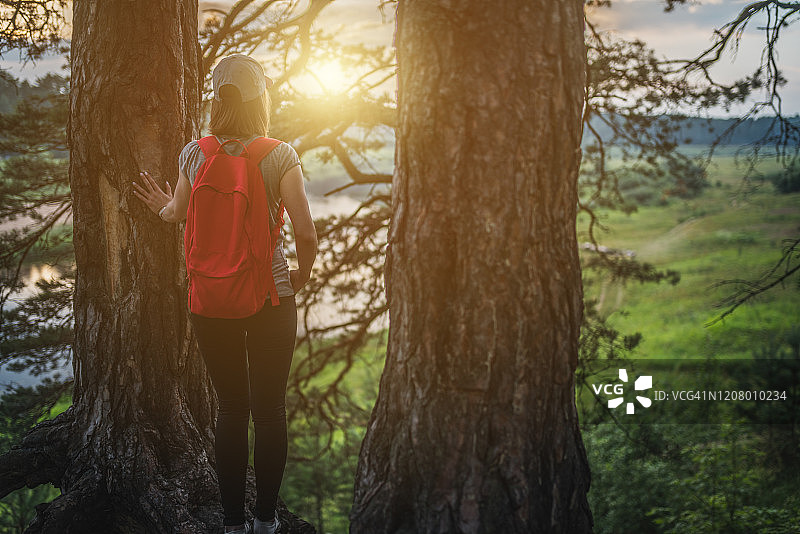 一个在树林里背着红色背包的年轻女人的后视图图片素材