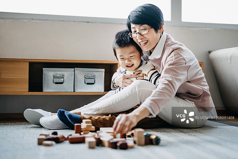 快乐的亚洲奶奶坐在客厅的地板上和小孙子一起玩积木图片素材