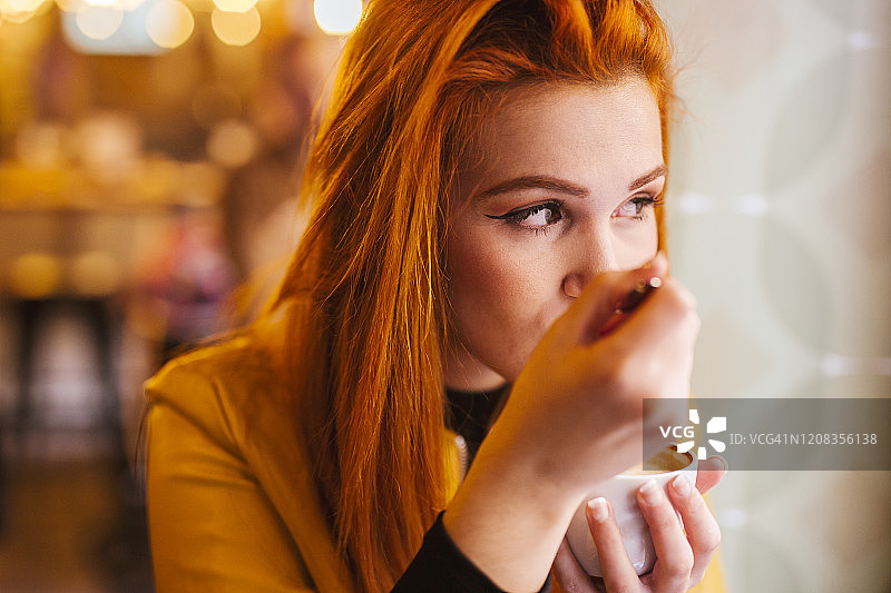 一幅红发年轻女子在咖啡店享用卡布奇诺的肖像图片素材