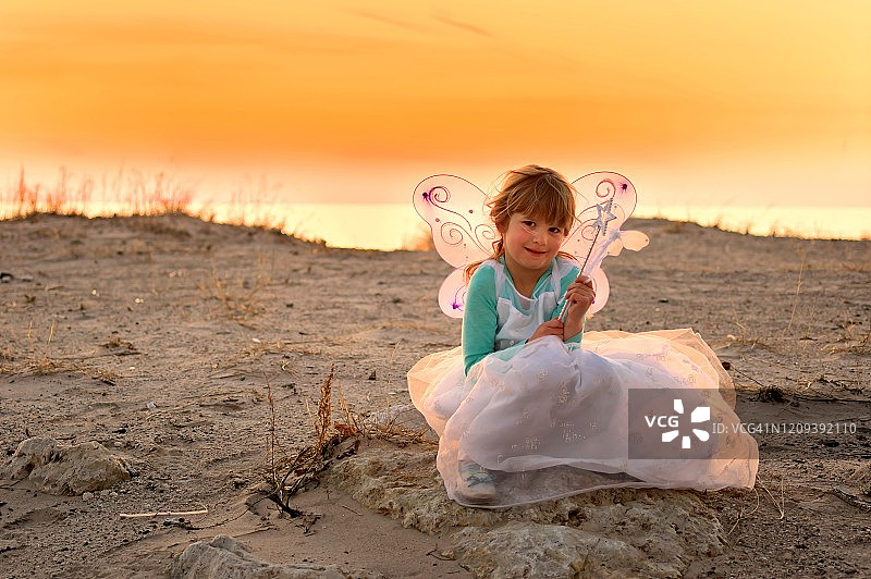 一个年轻女孩打扮成仙女坐在日落的海滩上的肖像图片素材