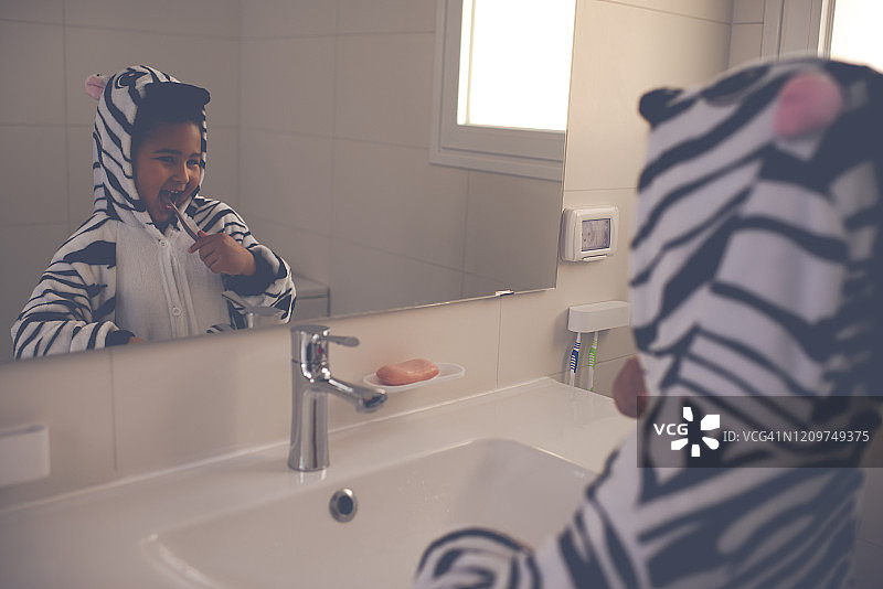 一个穿着斑马睡衣的小孩在浴室刷牙。图片素材