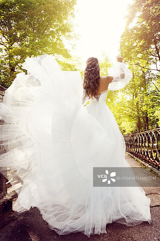 新娘后视图，快乐的女人穿着优雅的婚纱在夏季公园散步图片素材