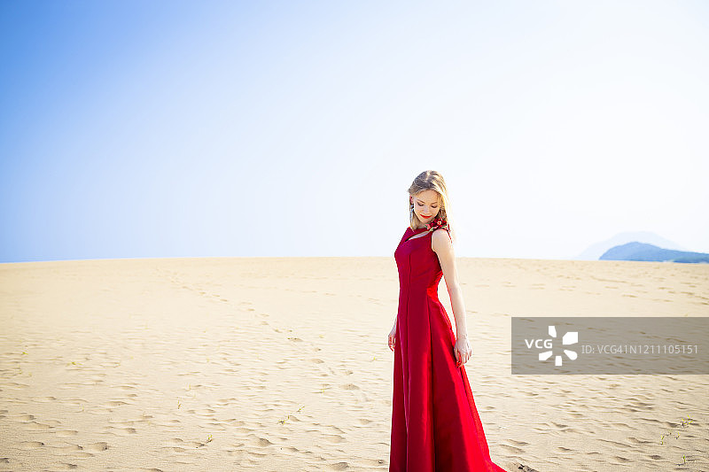 一个穿着红色衣服的白人女人站在沙丘上。图片素材