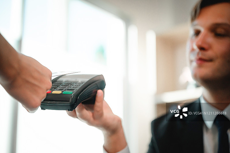 客户使用NFC技术的非接触式信用卡付款。手持信用卡读卡机的商人图片素材
