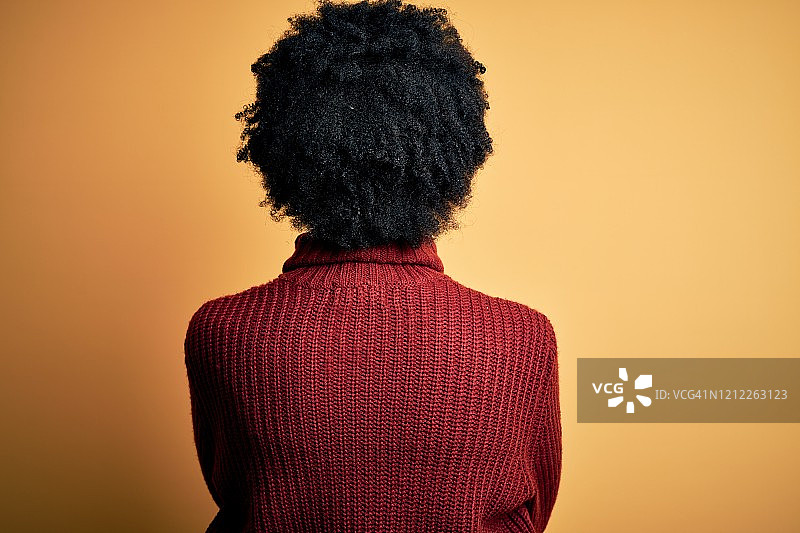年轻美丽的非洲裔美国妇女与卷发穿着休闲高领毛衣站向后看远离交叉双臂图片素材