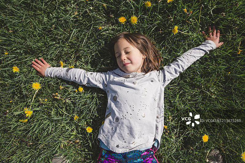 一个快乐的孩子躺在一片野花丛中，闭着眼睛图片素材