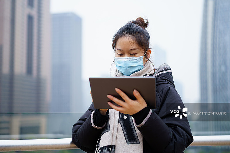 亚洲妇女使用数字平板电脑和保护面罩在街上图片素材