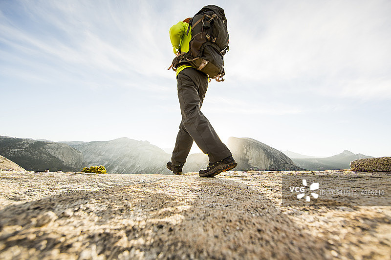 一名男子背包穿越一座多石的小山，远处有半圆丘。图片素材