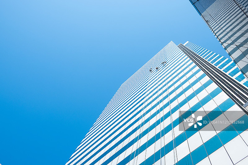 一组工人清洁高层建筑摩天大楼的窗户在蓝色的天空图片素材