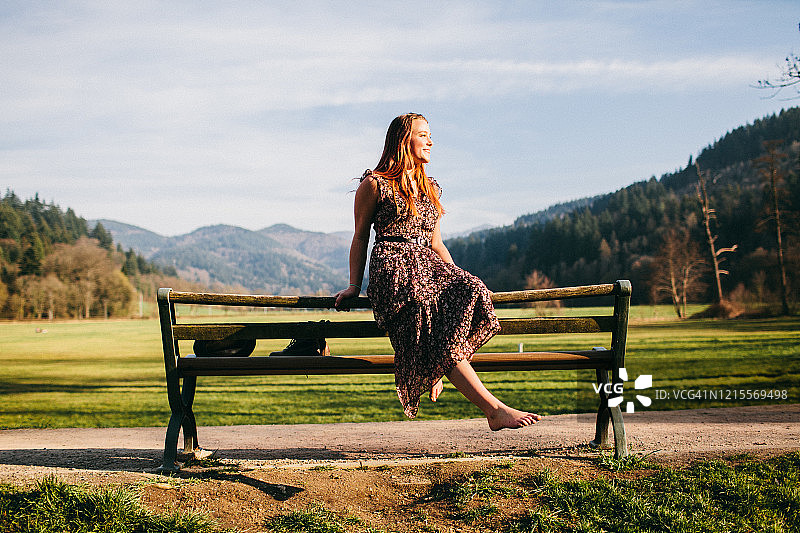 年轻女子赤脚坐在大自然的长椅上，面带微笑图片素材