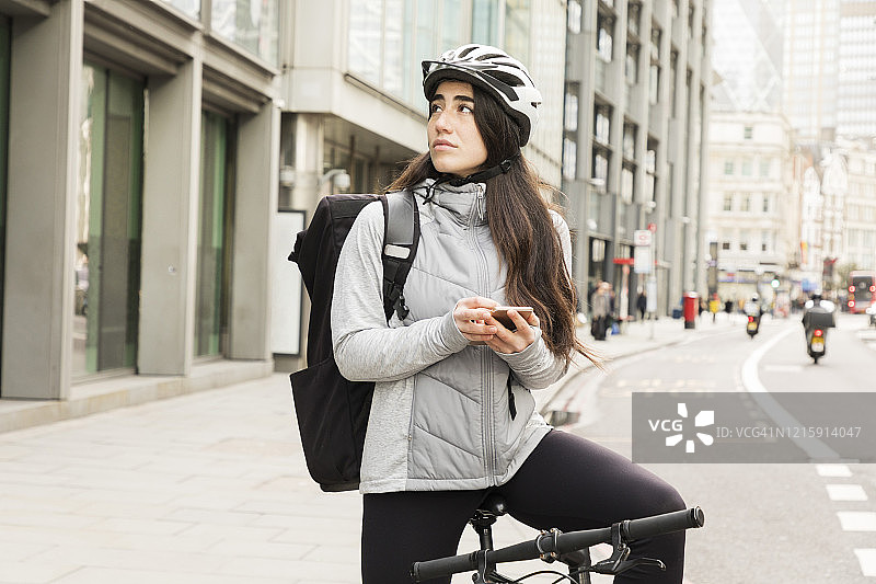 自行车上的女快递员用手机检查送货地址。图片素材