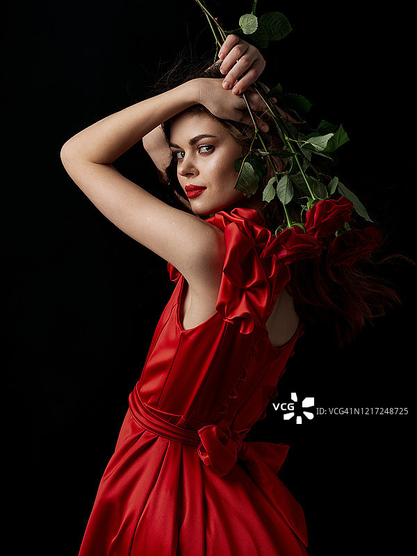 一个穿着红色晚礼服的女人手里拿着一束玫瑰花。图片素材