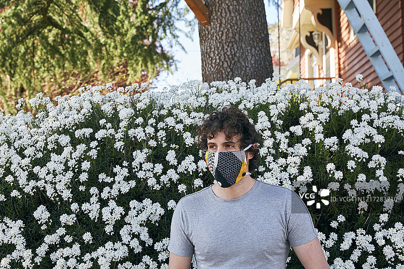 一个男人的肖像，在盛开的灌木与白花，戴着一个家庭缝面罩。图片素材