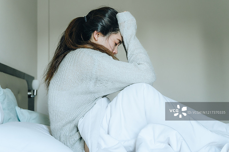 新冠肺炎大流行期间，抑郁的女性独自坐在卧室的床上，自我隔离。图片素材
