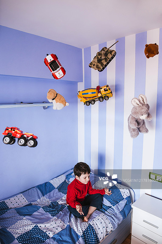 小男孩在床上沉思，玩具在他头上飞来飞去图片素材