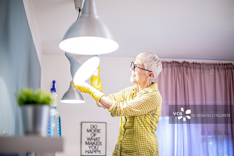 一位老妇人在擦拭一盏满是灰尘的灯。图片素材