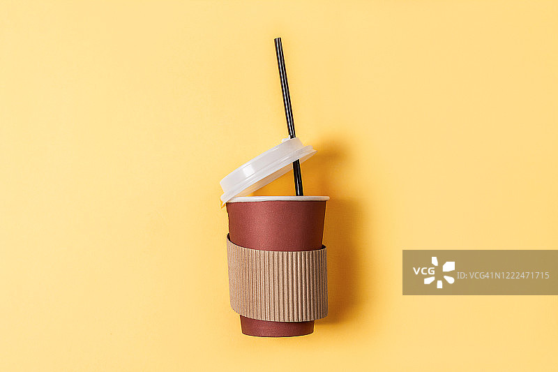 一次性纸杯咖啡在一个柔和的黄色背景。平的风格。纸杯咖啡图片素材