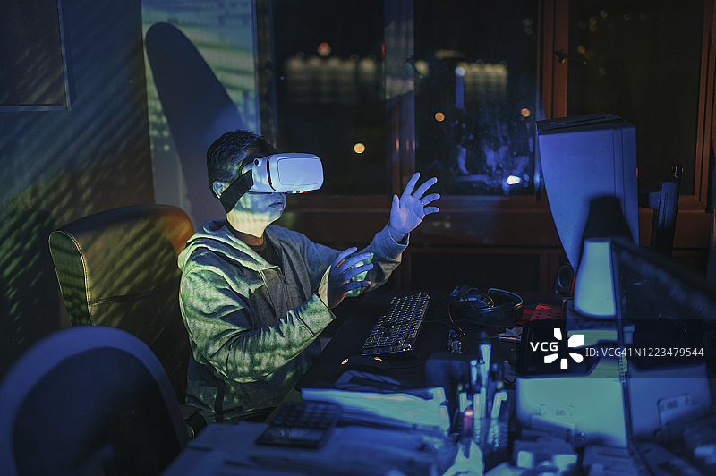 一名亚洲华人男性戴上VR眼镜，在他的家庭办公室自修室里，在他的台式电脑前体验3D虚拟游戏体验图片素材