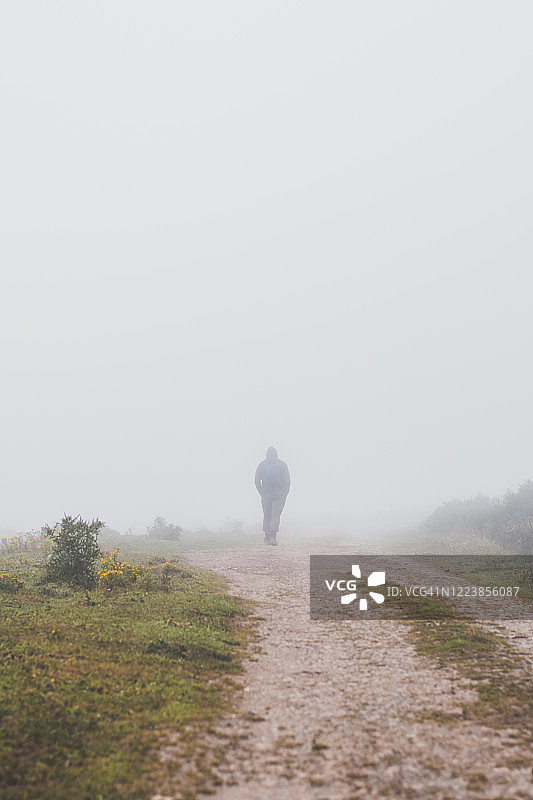 西班牙，坎塔布里亚，一个孤独男子的剪影，走在笼罩在雾中的乡间土路上图片素材