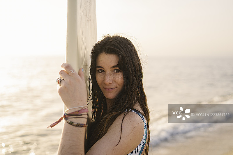 西班牙阿尔梅里亚海滩上微笑的年轻女子与冲浪板的肖像图片素材