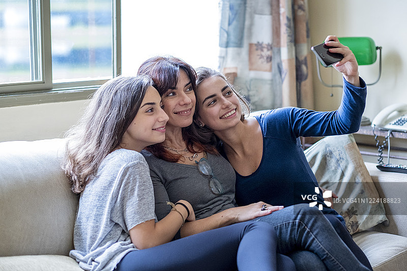 一位母亲和两个女儿一起坐在沙发上自拍图片素材