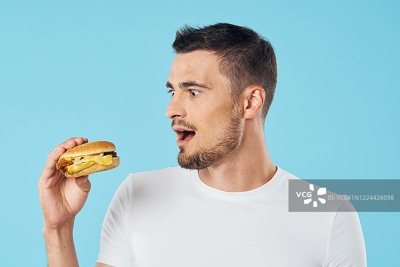 一个穿白色t恤的人咬了一个汉堡。图片素材