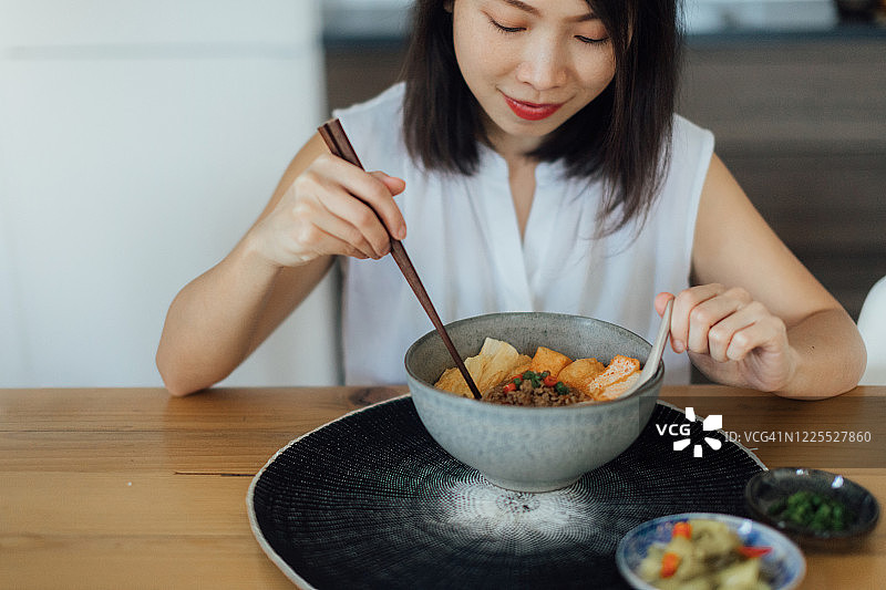 年轻的亚洲女子用筷子吃一碗新鲜的面汤图片素材