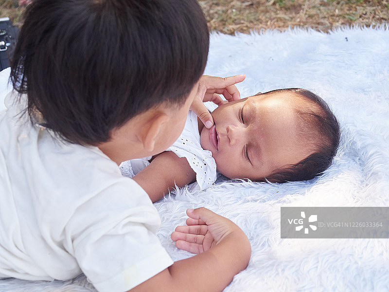 小弟弟摸他刚出生的妹妹。在户外公园。可爱的男孩和新生的女婴躺在白色的床上。图片素材