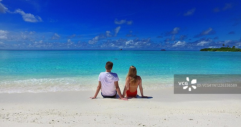后视图的幸福夫妇坐在海滩上看无尽的大海，享受风景在一个美丽的阳光明媚的日子与晴朗的天空图片素材