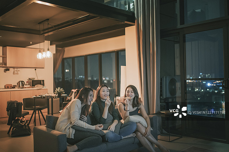 3个亚洲中国女人周五晚上聚集在公寓，看电视，看电影，坐在沙发上吃零食，享受每个公司图片素材