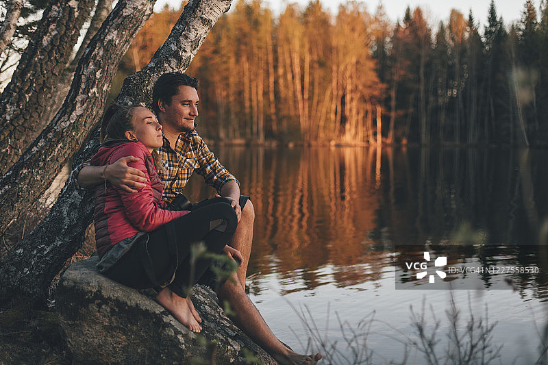 一对年轻夫妇坐在湖边的石头上看日落图片素材