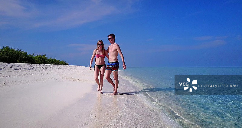 一对年轻的游客夫妇在马尔代夫的热带海滩上手拉手散步图片素材