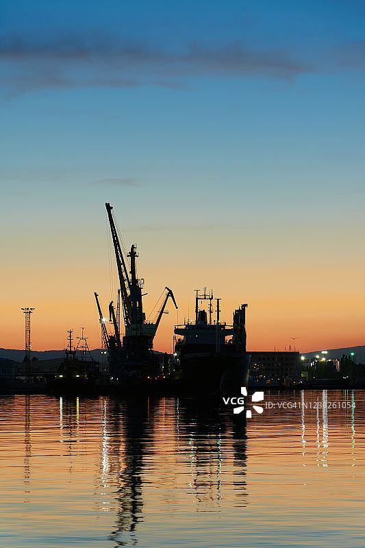 日落时分，起重机和船只停泊在港口图片素材