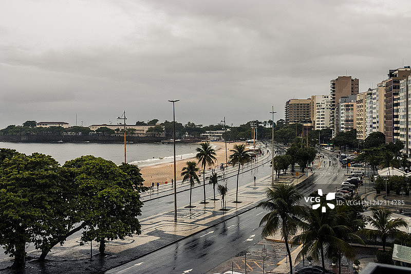 街道上的汽车和人们被树木、公寓、酒店、雨水、海滩和沙子包围着。图片素材