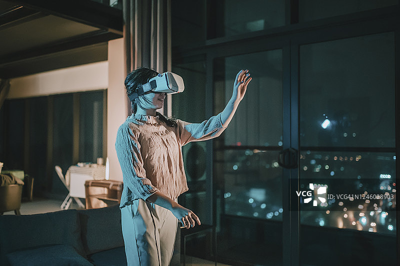 一位亚洲华裔少女戴上VR眼镜，在客厅体验3D虚拟游戏体验图片素材